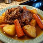 A close-up of a serving of tender pot roast with chunks of carrots and potatoes in a rich gravy.
