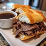Close-up of a delicious French Dip Sandwich piled high with shredded beef on a toasted bun, served with a side of au jus.