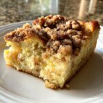 A close-up of a slice of French toast casserole with a crumb topping on a white plate.