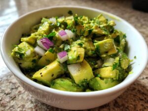 A bowl of fresh, chunky guacamole made with ripe avocados, diced red onion, and cilantro.