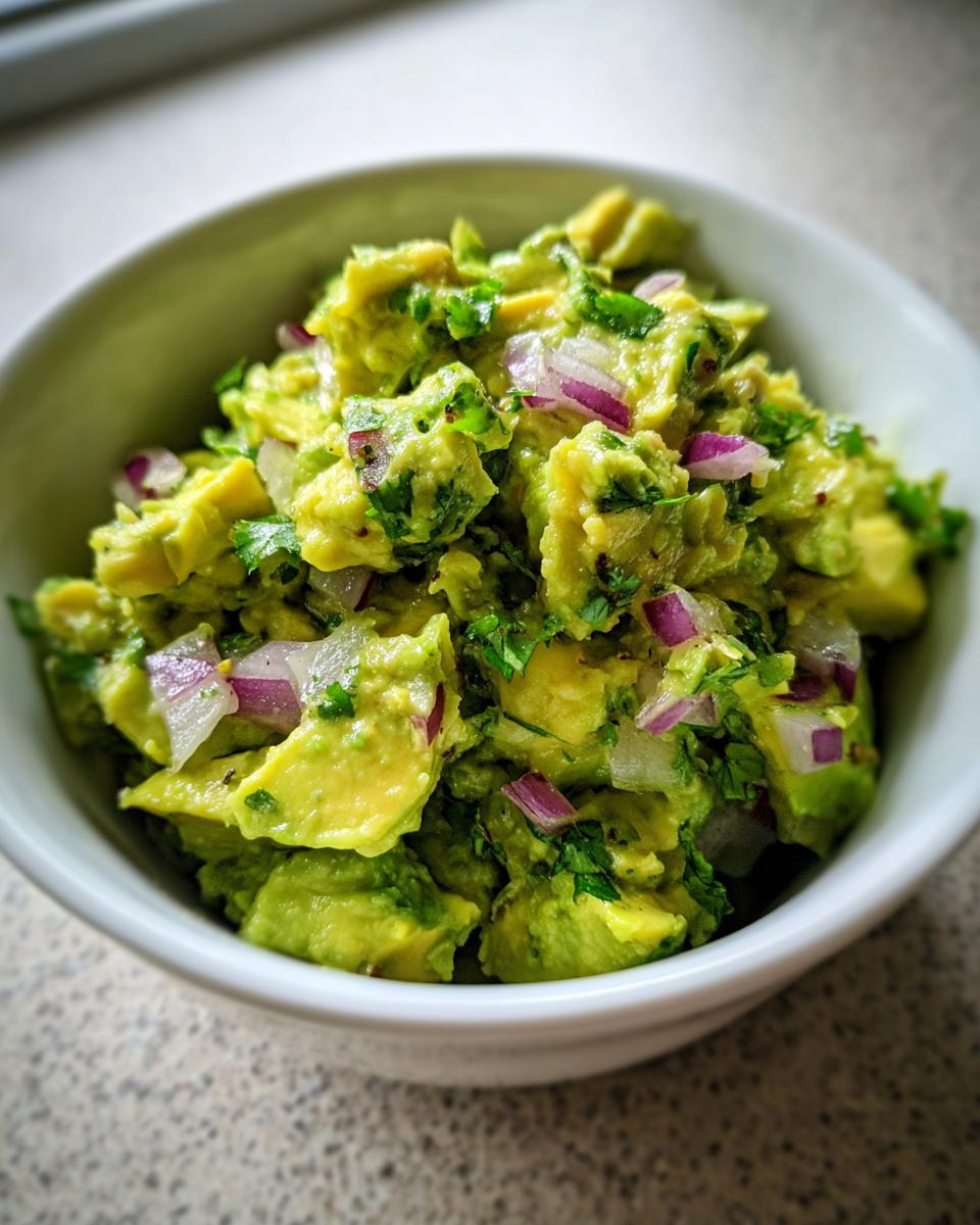 A close-up shot of a bowl of fresh guacamole, showcasing chunky avocado, diced red onion, and cilantro.