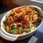 A close-up of a baked Green Bean Casserole in a white dish, topped with golden fried onions.