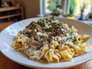 A close-up of creamy ground beef stroganoff served over wide egg noodles, garnished with fresh parsley.