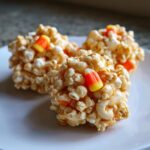 Close-up of three homemade Halloween Popcorn Balls decorated with candy corn on a white plate.