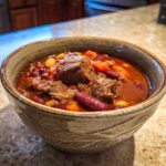 A close-up of a bowl filled with hearty beef chili, featuring tender chunks of beef, kidney beans, and carrots in a rich sauce.