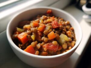 A close-up of a white bowl filled with hearty lentil soup, featuring lentils, carrots, celery, and tomatoes.