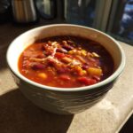 A close-up of a bowl filled with hearty vegetarian chili, featuring kidney beans, corn, and tomatoes.