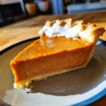 A delicious slice of homemade pumpkin pie, topped with whipped cream, on a plate.