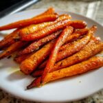 A close-up of glistening Honey Butter Roasted Carrots piled high on a white plate.