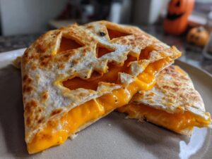 Close-up of a delicious Jack-o'-lantern Quesadilla, cut in half to reveal gooey melted cheese.
