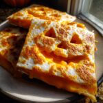 Close-up of a stack of golden-brown Jack-o'-lantern Quesadillas, featuring carved faces and melted cheese.