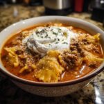 A close-up of a bowl of hearty Lasagna Soup, topped with a dollop of ricotta cheese and herbs.