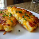Close-up of two golden-brown leftover mashed potato pancakes topped with melted cheddar cheese and chopped chives.