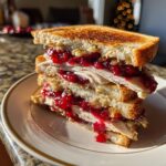 A tall, stacked leftover turkey sandwich with toasted bread, sliced turkey, and generous amounts of cranberry sauce.
