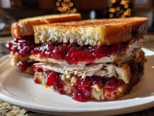 A close-up of a hearty leftover turkey sandwich piled high with sliced turkey and cranberry sauce on toasted bread.