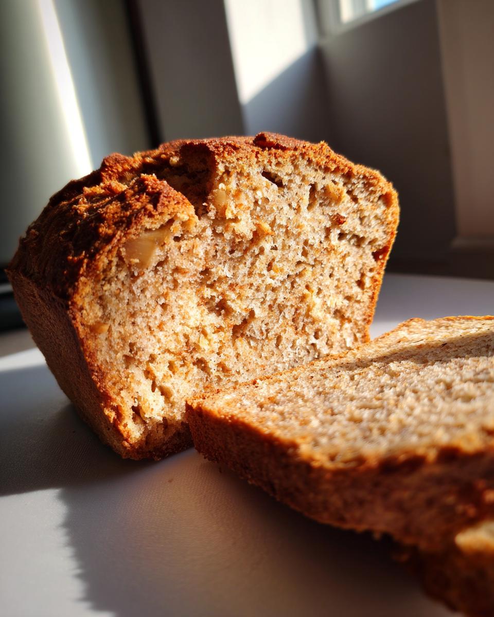 A close-up of a moist apple bread loaf with one slice cut and placed next to it, showing the texture and golden crust.