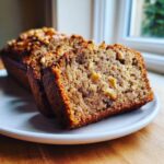 Close-up of a moist slice of banana bread with walnuts, showcasing its texture and nutty inclusions.