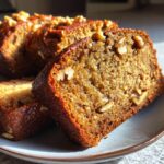 Close-up of a slice of moist banana bread studded with walnuts, served on a plate.