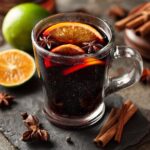 A steaming mug of mulled wine garnished with orange slices, star anise, and cinnamon sticks.