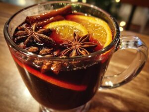 A close-up of a glass mug filled with warm mulled wine, garnished with orange slices, star anise, and cinnamon sticks.