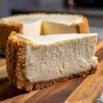 A close-up view of a slice of creamy no bake cheesecake with a graham cracker crust on a wooden board.