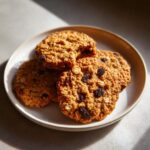A close-up of four delicious Oatmeal Raisin Cookies stacked on a plate, with visible oats and raisins.