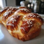 Close-up of a golden-brown Pan de Muerto bread, braided and sprinkled with sugar crystals.