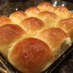 A close-up of freshly baked Parker House rolls, glistening with butter in a glass baking dish.