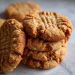 A close-up stack of delicious peanut butter cookies, sprinkled with sea salt, showing classic fork marks.