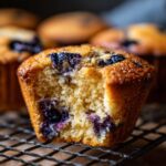 Close-up of a perfect blueberry muffin with a bite taken out, showing juicy blueberries and fluffy texture.