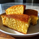 Three golden-brown slices of delicious cornbread stacked on a white plate.