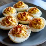 A plate of perfectly prepared deviled eggs, generously filled and sprinkled with paprika.