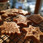 Close-up of perfectly baked gingerbread cookies in snowflake and geometric shapes cooling on a wire rack.