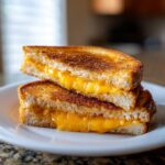 A close-up of a perfect grilled cheese sandwich, cut in half and stacked, showing melted golden cheese oozing out.