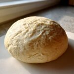 A perfectly formed ball of pizza dough, ready for baking, with a slightly textured surface.