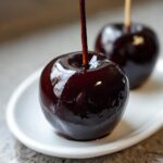 Close-up of two glossy, dark Poison Candy Apples on a white plate, ready for Halloween.