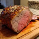 A perfectly cooked prime rib roast with a golden-brown crust and juicy pink interior, sliced on a wooden cutting board.