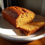 A close-up of a rustic Pumpkin Beer Bread loaf with one slice cut, showcasing its moist crumb and golden-brown crust.