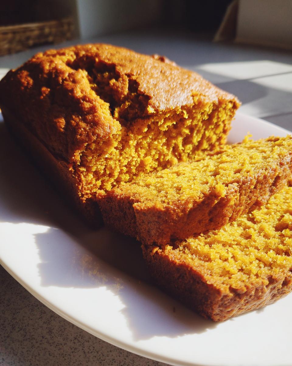 A close-up of a sliced loaf of moist Pumpkin Beer Bread on a white plate, bathed in sunlight.