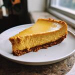 A perfect slice of rich and creamy Pumpkin Cheesecake on a white plate, showcasing its graham cracker crust.