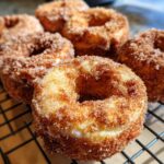 A close-up of several freshly baked Pumpkin Donuts coated in cinnamon sugar, resting on a cooling rack.