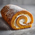 A close-up of a crack-free pumpkin roll dusted with powdered sugar, revealing a swirl of creamy filling.