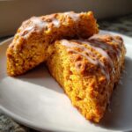 Close-up of two triangular Pumpkin Scones drizzled with white glaze on a white plate.