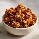 A bowl filled with crunchy Pumpkin Spice Granola clusters, featuring dried cranberries and pumpkin seeds.