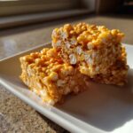 Close-up of two Pumpkin Spice Rice Krispie Treats stacked on a white plate, showing the texture of puffed rice and marshmallows.
