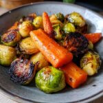 Close-up of a bowl filled with perfectly roasted brussels sprouts and carrots, glistening with seasoning.