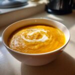 A bowl of vibrant orange Roasted Butternut Squash Soup with a swirl of cream on top.