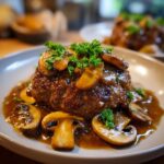 A close-up of a juicy Salisbury steak topped with sautéed mushrooms and rich gravy, garnished with fresh parsley.