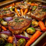 Close-up of juicy sheet pan pork chops with roasted Brussels sprouts, carrots, and red onion.