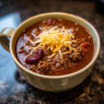 A close-up of a bowl of rich, hearty slow cooker chili topped with shredded cheddar cheese and kidney beans.